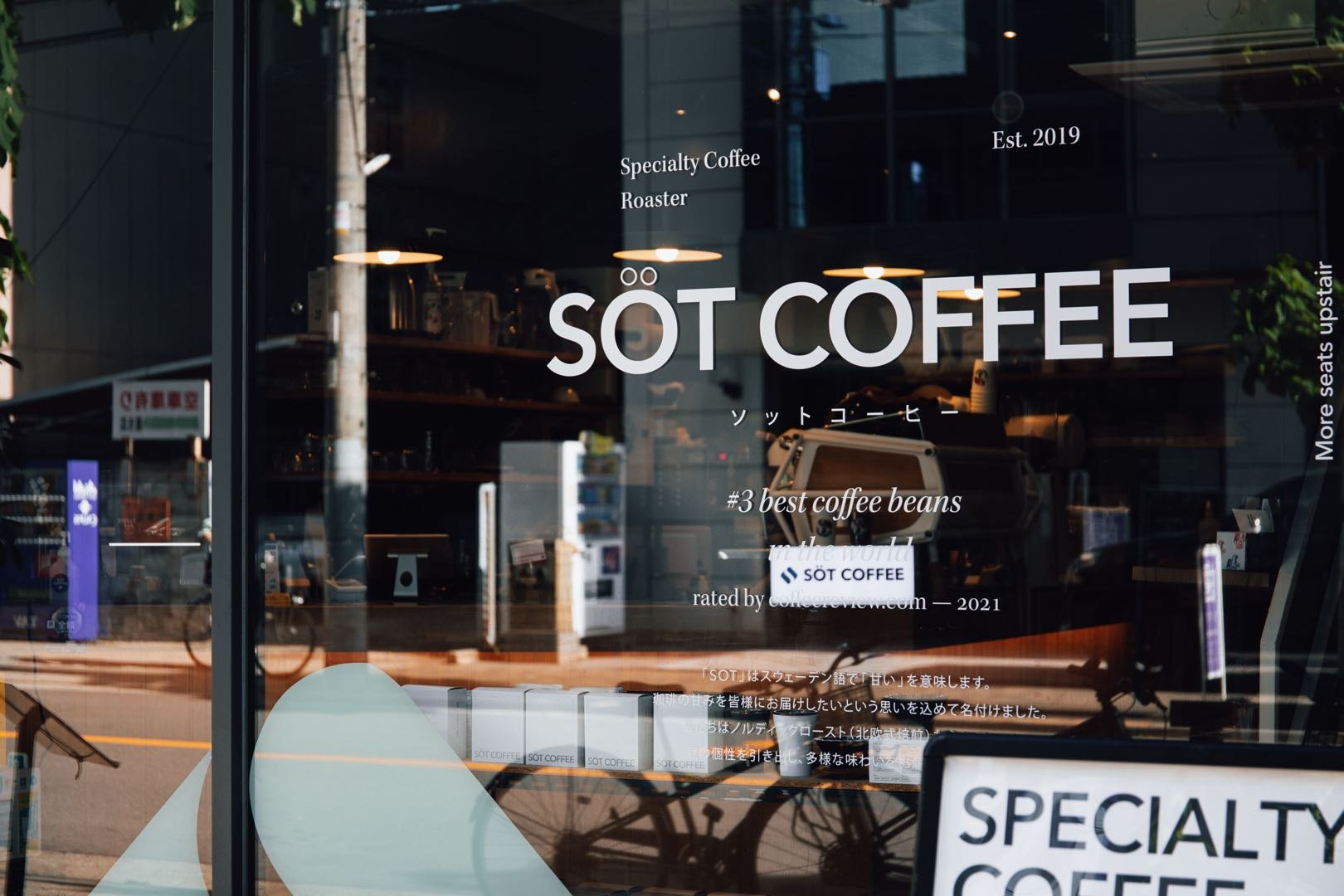 SÖT COFFEE ROASTERのガラス張りの店舗外観。店名ロゴ、店内のカウンター、通りに面したファサードが写っている。
